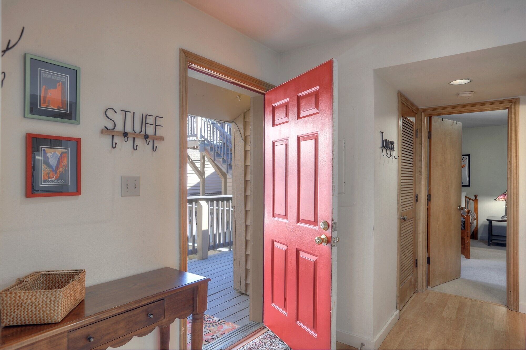 A hallway with a red door, a wooden bench, and framed pictures on the wall.