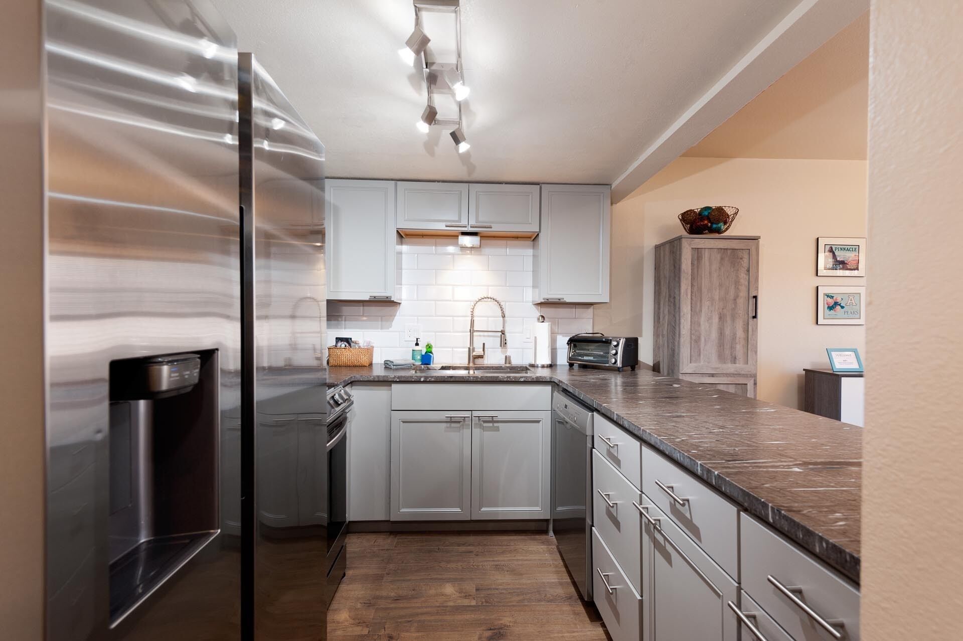Una cocina moderna con armarios blancos, un refrigerador de acero inoxidable, horno empotrado, un fregadero y un tostador.