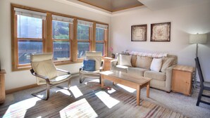 A living room with a sofa, two armchairs, a coffee table, and a lamp. There are three large windows providing natural light. - Village View Vista | Walk to Town, Pool/Hot Tub - Near FLC, Golf (Durango)