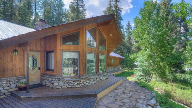 Une cabane en bois dotée de grandes fenêtres, d’une fondation en pierre et d’une terrasse en bois.