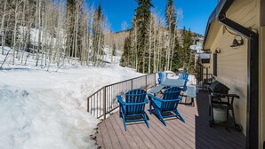 A wooden deck with blue Adirondack chairs, a barbecue grill, and a snow-covered landscape with trees. - Purgatory townhome with Easy Access to Slopes - Views - EV Charger (Durango)