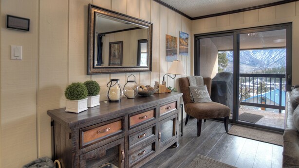 A living room with a wooden cabinet, a large mirror, and a view of a mountain through a sliding glass door. - Double Diamond | Walk to Ski Lift & Pool Access - Mtn Views, Fireplace (Durango)