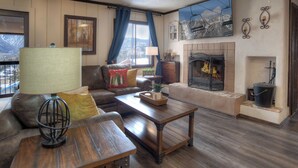 A cozy living room with a fireplace, leather sofa, wooden coffee table, and a view of mountains through the window. - Double Diamond | Walk to Ski Lift & Pool Access - Mtn Views, Fireplace (Durango)
