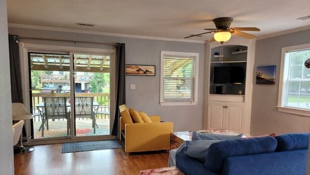Una sala de estar con sofá azul, sillón amarillo y televisor. Hay una puerta corrediza de vidrio que da a un área exterior con terraza.