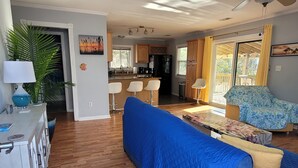 Una sala de estar con un sofá azul, un comedor con mesa y sillas, una cocina con armarios de madera y un ventanal con cortinas.