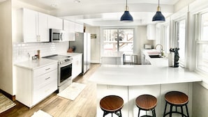 A modern kitchen with white cabinetry, a central island with stools, a microwave, and a stove. - 6 bedroom modern West Vail Home w/2 large decks, 300 yds from Vail free shuttle (Vail)