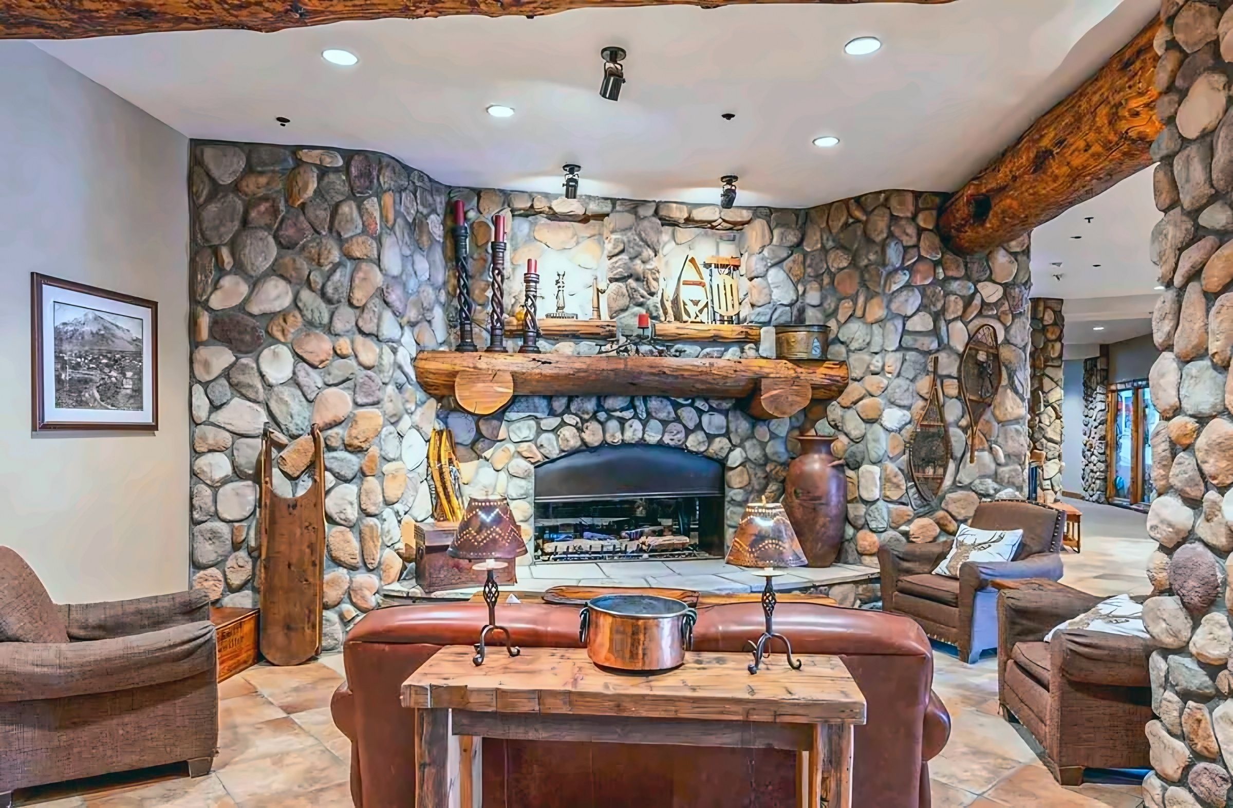 Une pièce aux murs de pierre, dotée d’une cheminée, de fauteuils en cuir et d’une table en bois.