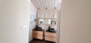 Une salle de bain avec un meuble-lavabo en bois, deux vasques sur colonne, un miroir et des luminaires suspendus.