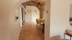Un couloir mène à une salle à manger dont le sol est carrelé et le plafond en bois.