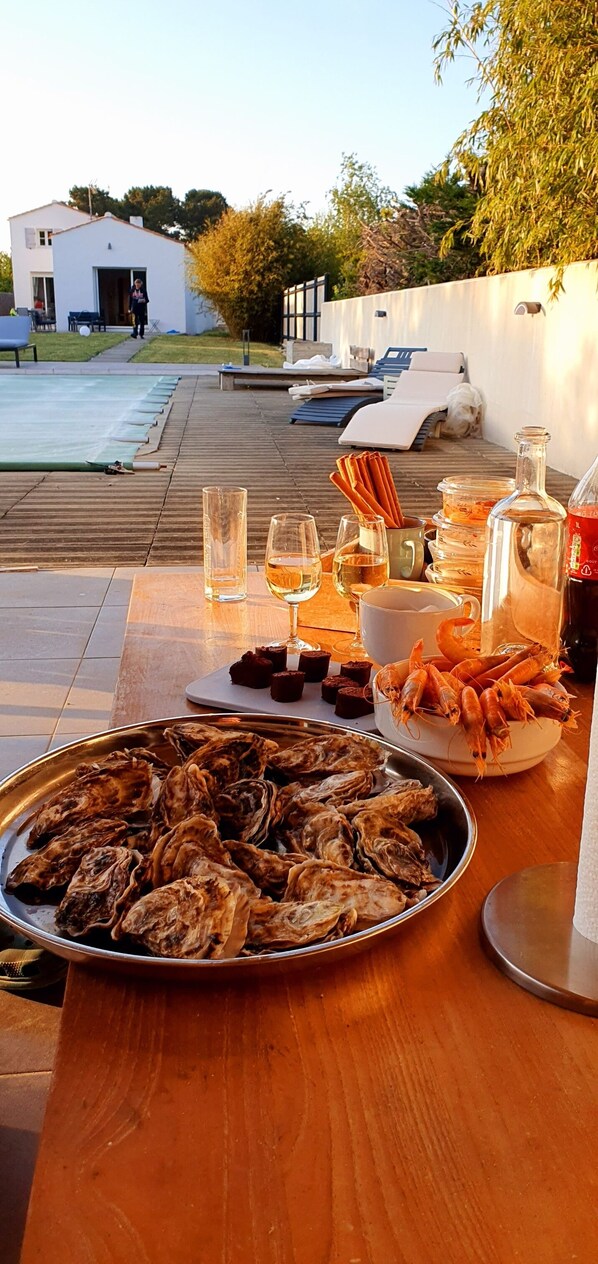 Un espace de restauration en plein air avec une table dressée pour un repas, comprenant des huîtres, des crevettes et des boissons.