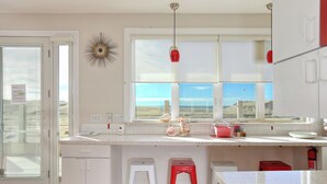 Una cocina con un gran ventanal, armarios blancos, una encimera y dos taburetes.