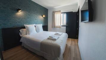 Une chambre d’hôtel avec un lit, un téléviseur à écran plat fixé au mur et une fenêtre avec des rideaux.