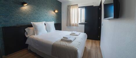 A hotel room with a bed, a flat-screen TV mounted on the wall, and a window with curtains.