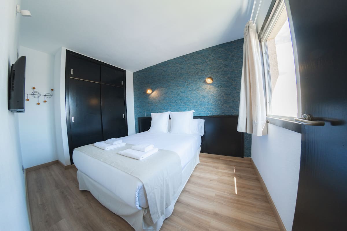 Quarto moderno com cama grande, guarda-roupa escuro e parede azul com textura.