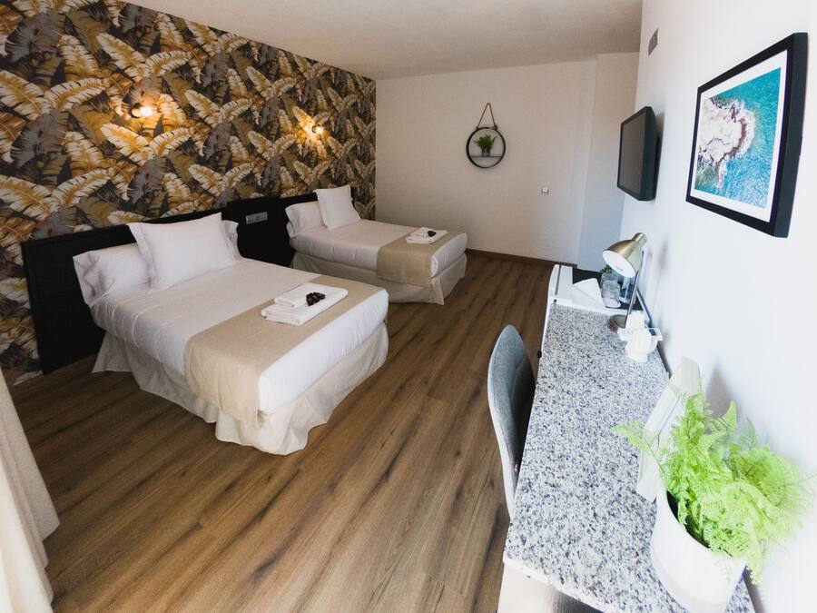 A hotel room with two beds, a small desk, a wall-mounted TV, and a framed picture.