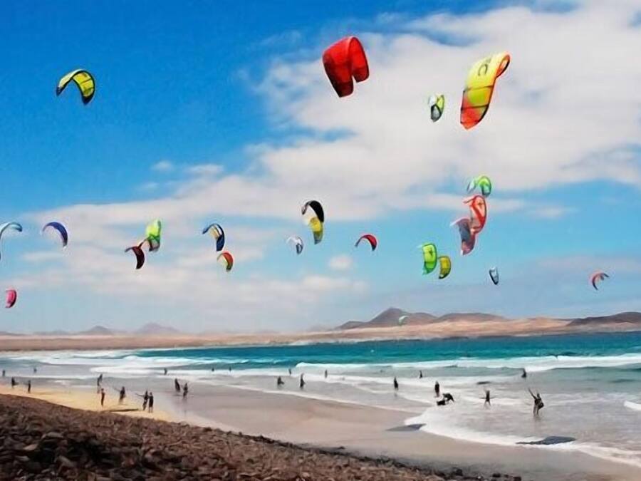 A beach with people and kites flying in the sky.