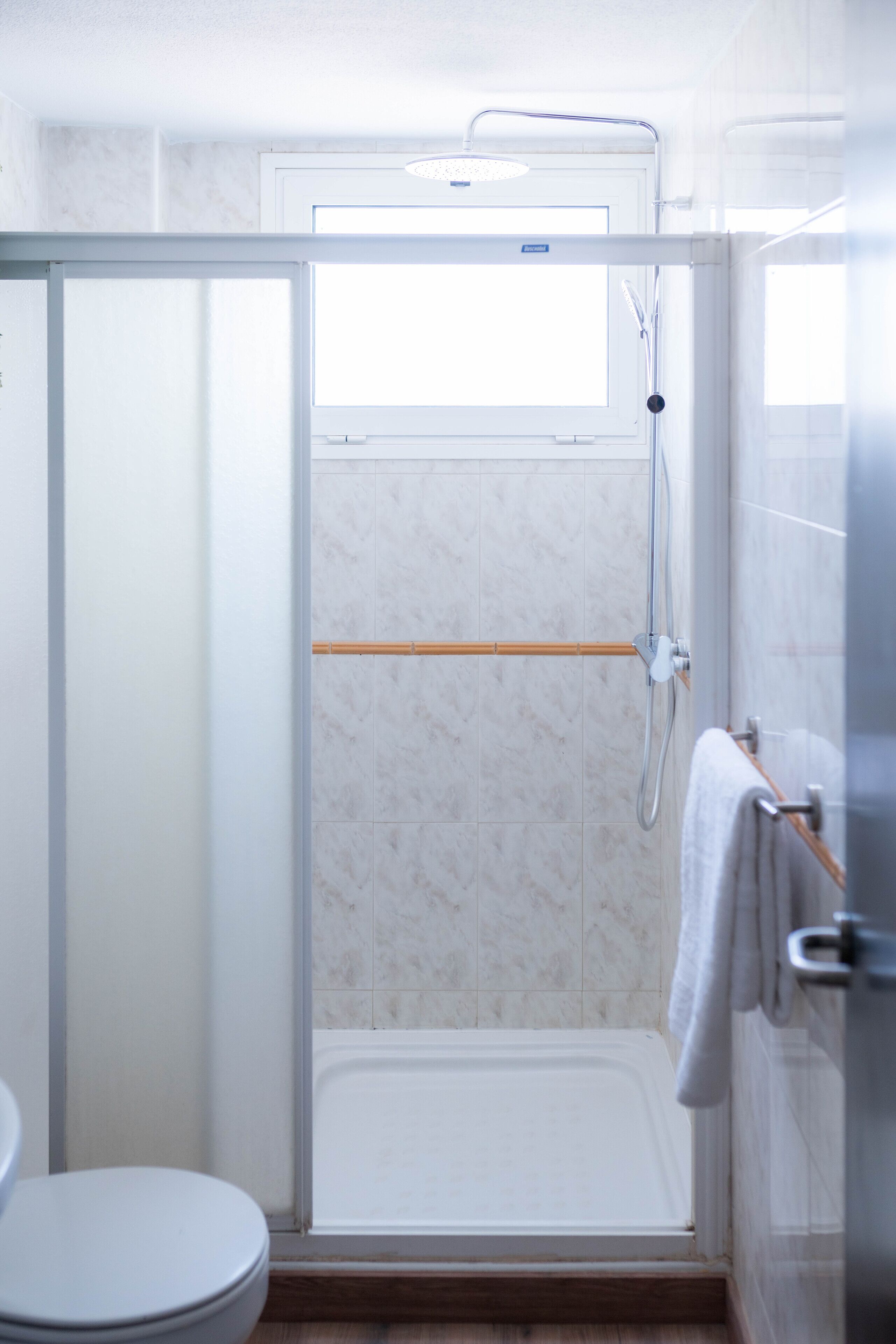 Una doccia con porta in vetro, una vasca da bagno bianca e un portasciugamani in legno.