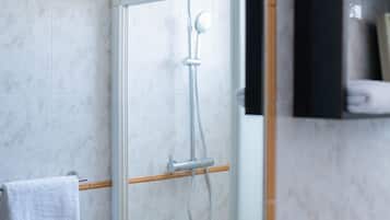 A modern bathroom with a glass-enclosed shower, a white towel hanging on the wall, and a wooden shelf with toiletries.