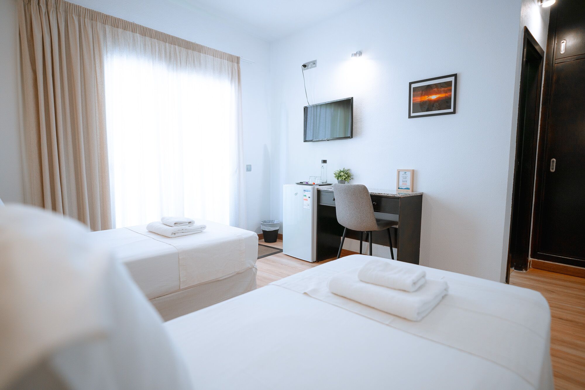 Une chambre d’hôtel avec deux lits, un bureau, une chaise, une télévision et un tableau au mur.