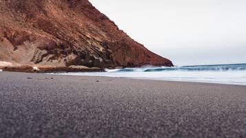 A beach with a rocky cliff and waves crashing onto the shore.