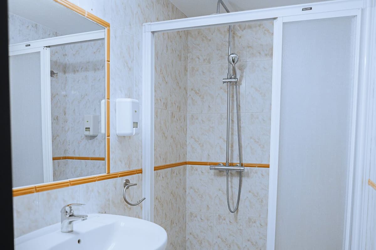 Casa de banho com lavatório branco, cabine de duche e espelho com moldura dourada.