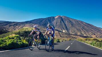 Two cyclists on a road with a mountain in the background.