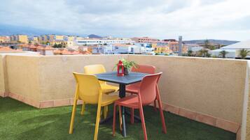A rooftop terrace with a table and chairs, a potted plant, and a view of a coastal town.