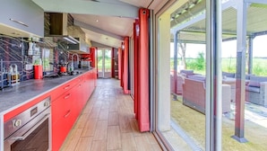 A modern kitchen with red cabinetry and a view to an outdoor patio area. - Belle Quercynoise with private Hammam and jacuzzi (Septfonds)