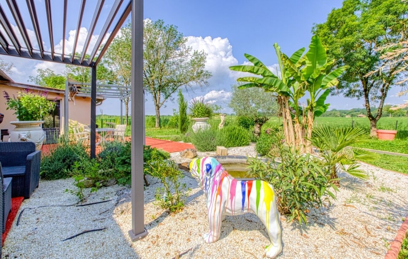 En trädgård med en dekorativ hundstaty, en pergola och en sittplats med utemöbler.