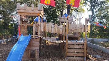 Une structure de jeux en bois, dotée d’un toboggan bleu, d’éléments d’escalade et de drapeaux.
