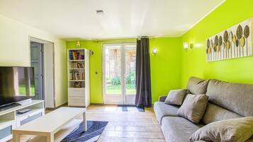 A living room with a sofa, TV, bookshelf, and a door leading to a balcony.