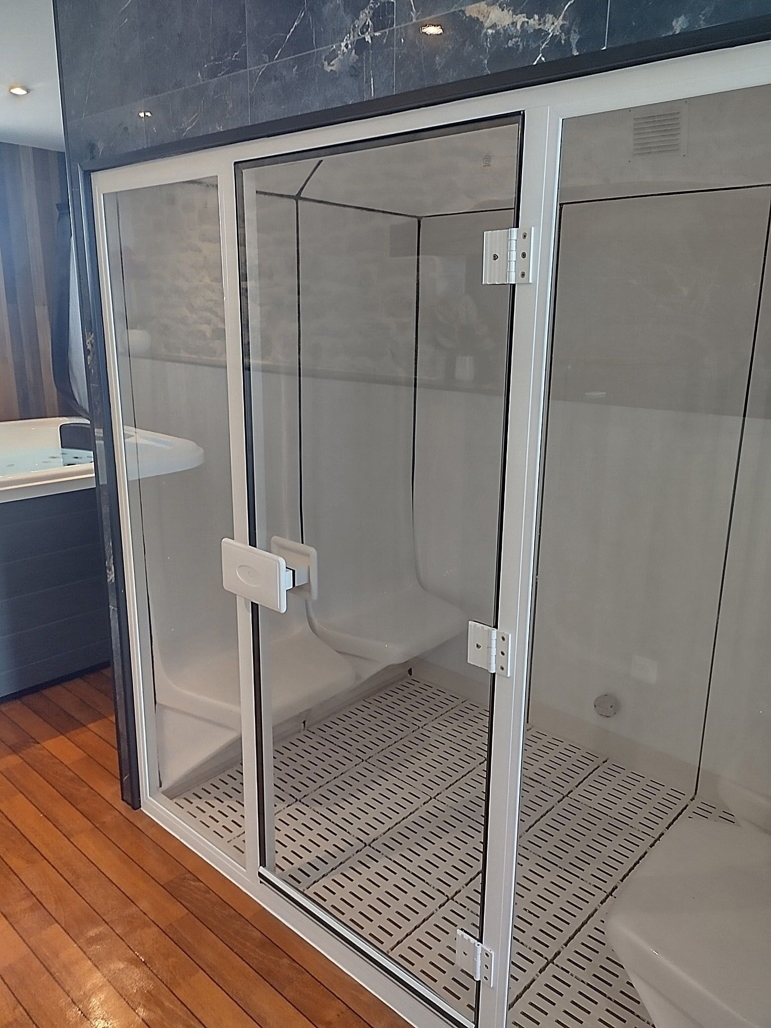Un cerramiento de ducha con puerta de vidrio, marco metálico y sistema de ventilación.