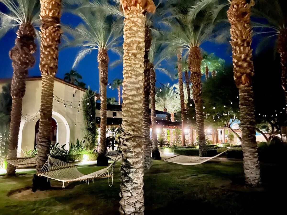 Vista nocturna de un resort con palmeras, una hamaca y un edificio con arcos.