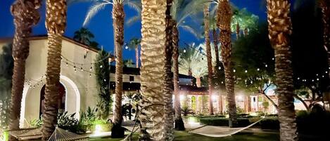 Vista nocturna de un resort con palmeras, una hamaca y un edificio con arcos.