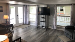 Ein Wohnzimmer mit Flachbildfernseher auf einem Schrank, einem dunklen Holztisch, einer Lampe und einem Sofa.