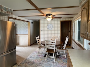 Een keuken met een eettafel, stoelen, een koelkast, een plafondventilator en een klok aan de muur.