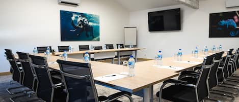 A conference room with a long table, black chairs, water bottles, and two large paintings on the walls.
