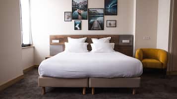 Una cama grande con cabecera de madera, varios almohadones y un sillón amarillo pequeño en una habitación de hotel.