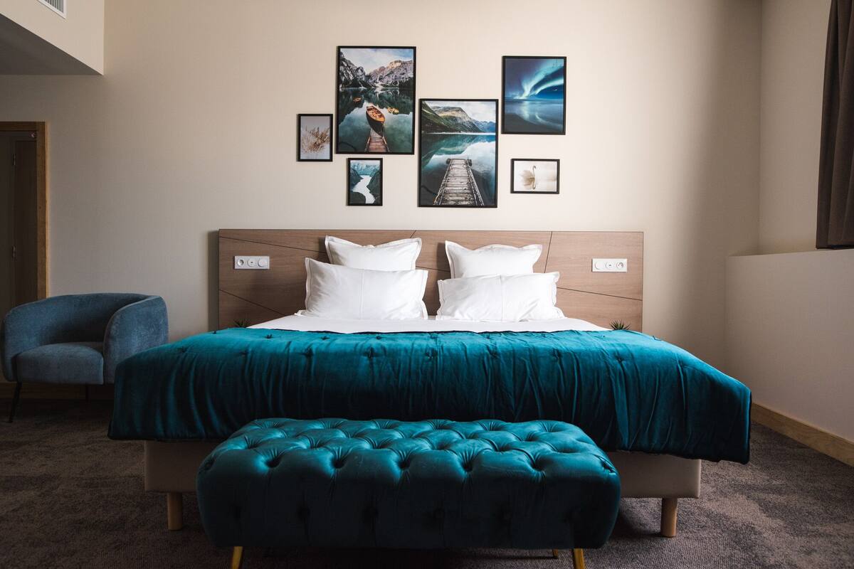 Quarto de hotel com uma cama grande, um banco acolchoado azul e uma parede decorada com quadros.