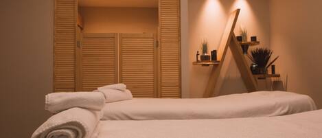 A bedroom with two beds, a wooden wardrobe, and a bedside table with a mirror and plants.
