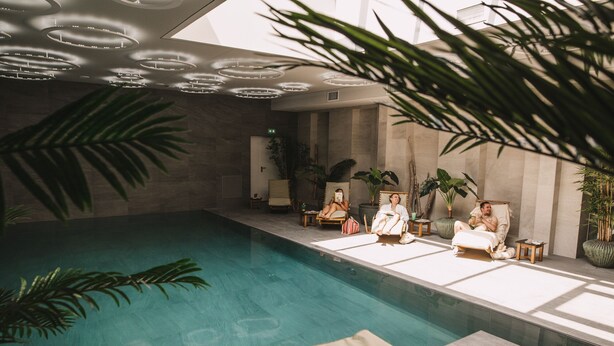 Un espace piscine doté de chaises longues et d’un plafond orné de luminaires circulaires.