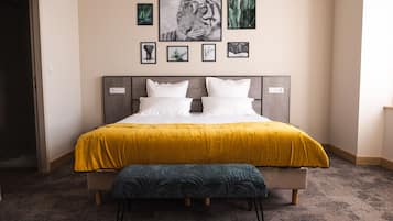 Una cama bien tendida con un edredón amarillo y un banco a juego, un cabecero con toma de corriente y varias fotografías enmarcadas en la pared sobre la cama.