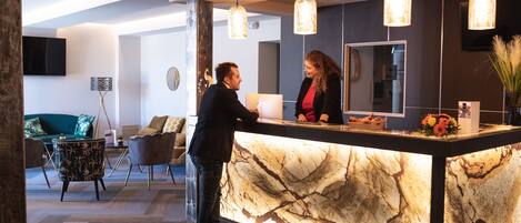 A reception desk with a marble top, pendant lights, and a mirror above it.