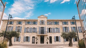 Un bâtiment en pierre doté de nombreuses fenêtres et volets, une entrée centrale et un balcon.