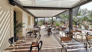 Un espace extérieur aménagé pour les repas, avec des tables et des chaises, une pergola offrant de l’ombre et une vue sur le jardin environnant.