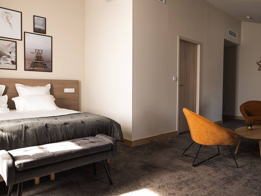 Ein Hotelzimmer mit einem Bett, einer Sitzbank, zwei Stühlen und einer Tür zu einem weiteren Raum.