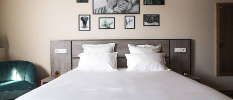 A bedroom with a large bed, two white pillows, a grey headboard, and a teal armchair.