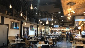 Un restaurant spacieux avec de nombreuses tables et chaises, des luminaires suspendus et un bar situé au fond de la salle.