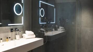 A modern bathroom with a glass shower enclosure, a large mirror with illuminated frames, and a white vanity with a sink and towel rack.