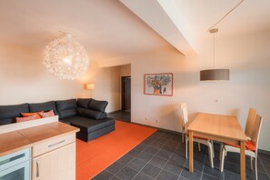 Un salon moderne comprenant un canapé, une table à manger avec des chaises, un coin cuisine et un luminaire sphérique original.